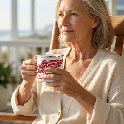 Woman age 65–75 relaxing on a coastal porch holding a stainless steel enamel camping mug with red ‘Born to Be a Senior’ design.