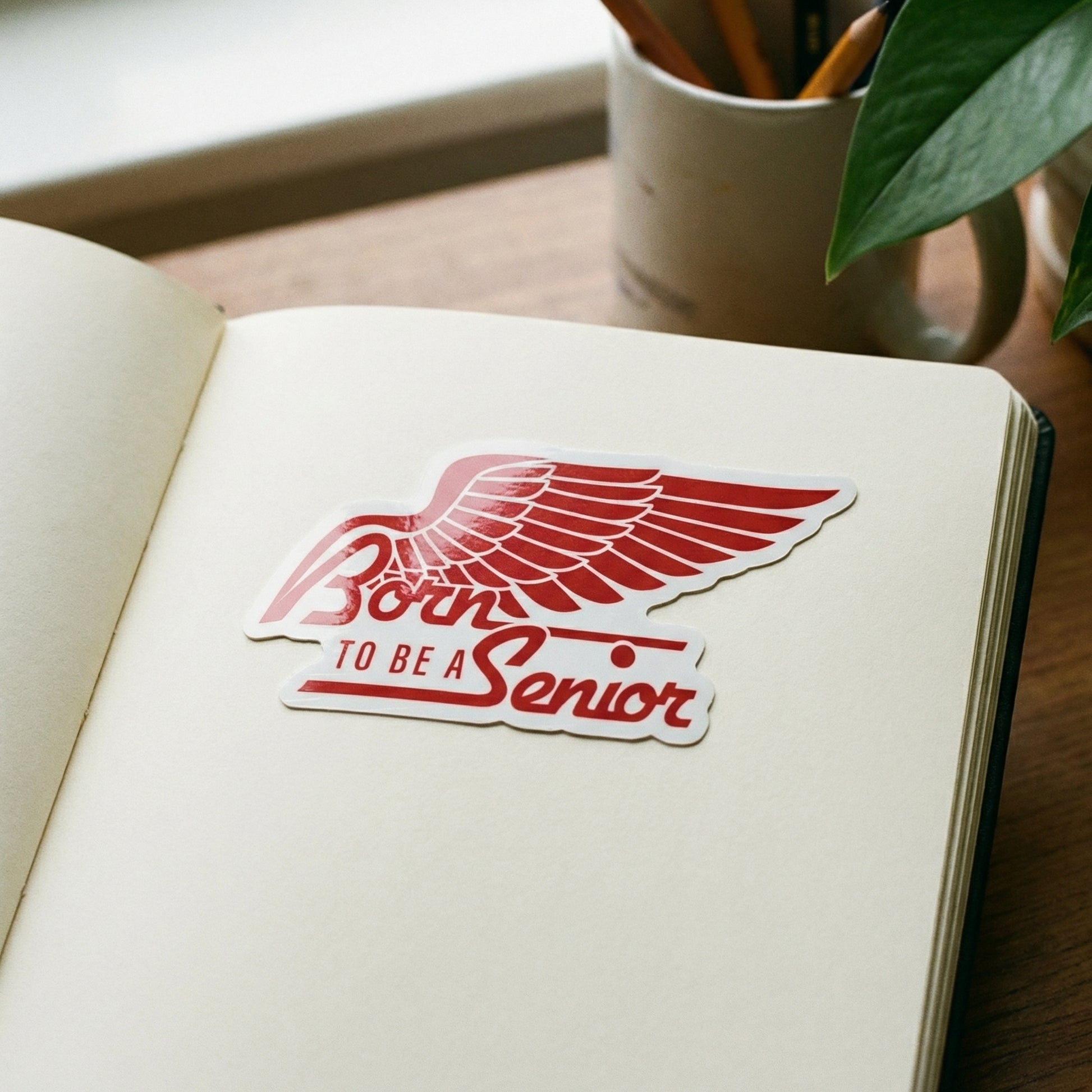 Open notebook with a red 'Born to be a Senior' Magnet on a wooden surface.