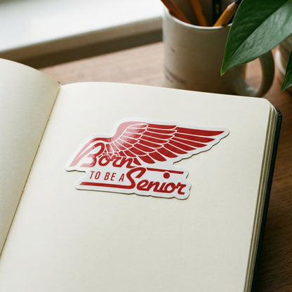 Open notebook with a red 'Born to be a Senior' Magnet on a wooden surface.