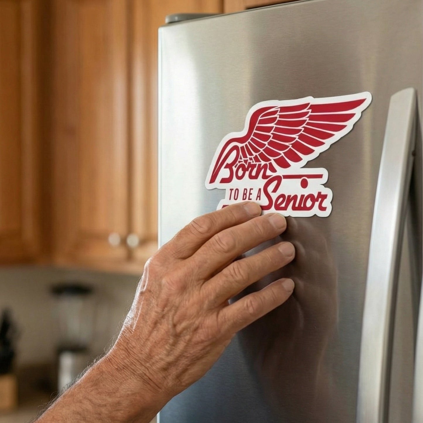 Hand placing a ‘Born to Be a Senior’ die cut magnet on a stainless steel refrigerator in a home kitchen