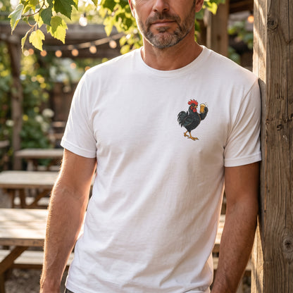 Man wearing the white Brewed Awakening T-shirt with a small beer-drinking rooster graphic on the left chest, standing outdoors by a wooden post.